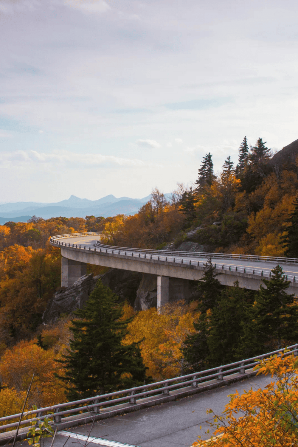 Vivid autumn landscape with mountain bridge, colorful fall foliage, scenic mountain highway, QuestForDirections outdoor travel image.