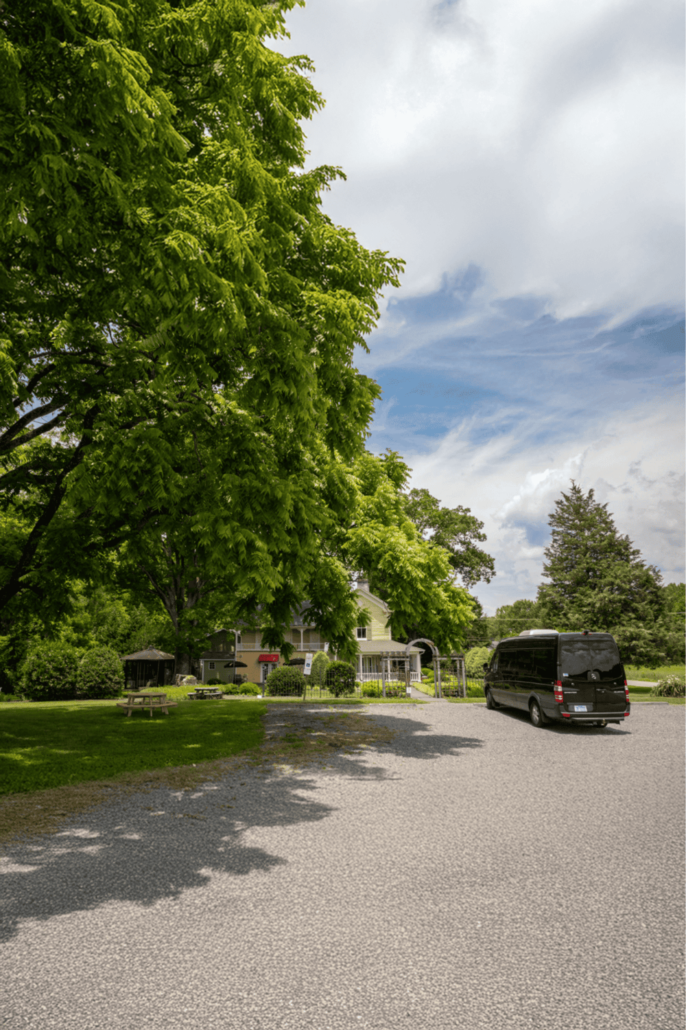 Lush green trees and a parking area with a van in front of a cozy building on QuestForDirections site.