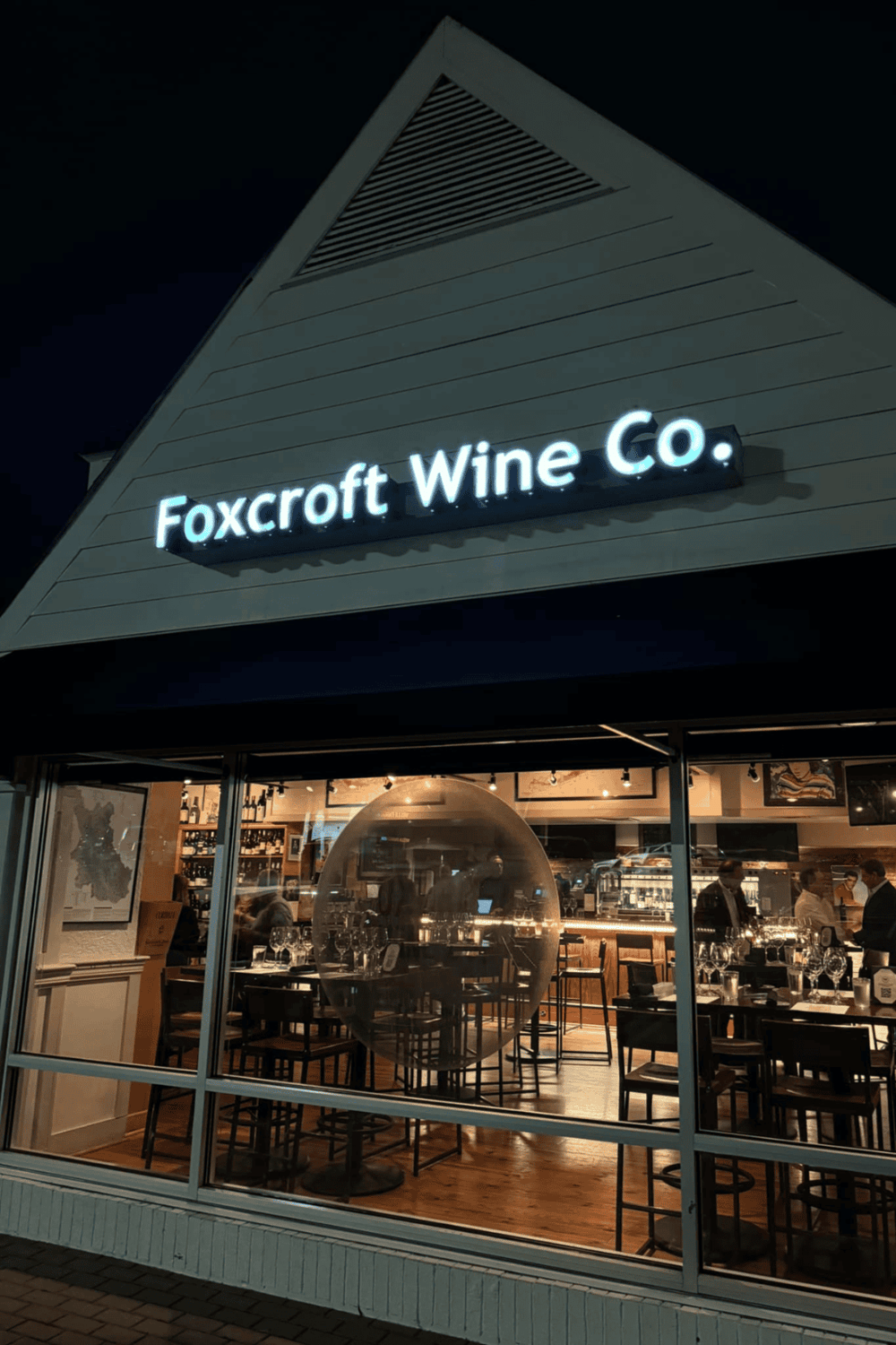 Elegant winery storefront at night with illuminated sign and modern interior decor.