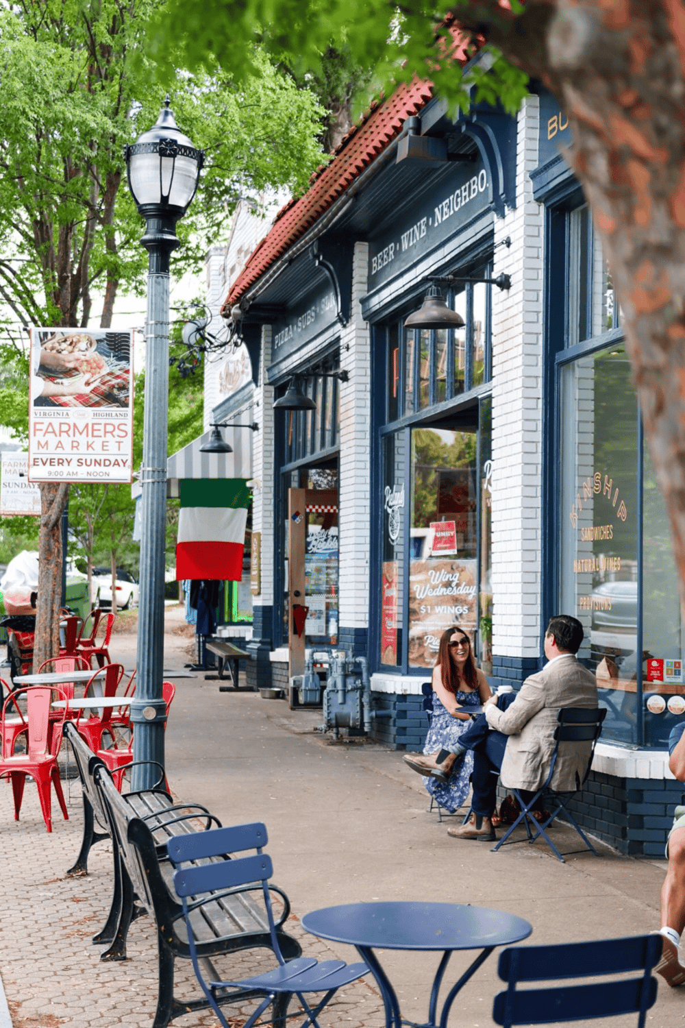 Quiet outdoor dining at a trendy pizza shop on a lively city street with trees and colorful chairs.