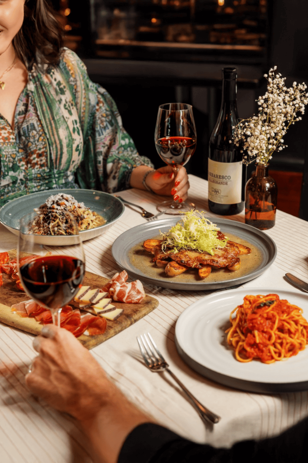 Elegant dinner with wine, pasta, and charcuterie at a cozy restaurant, ideal for food and wine lovers.