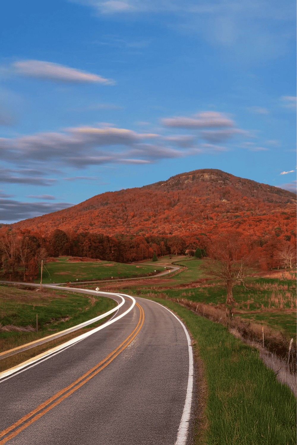 Rolling mountain road with autumn foliage and scenic landscape in the background.
