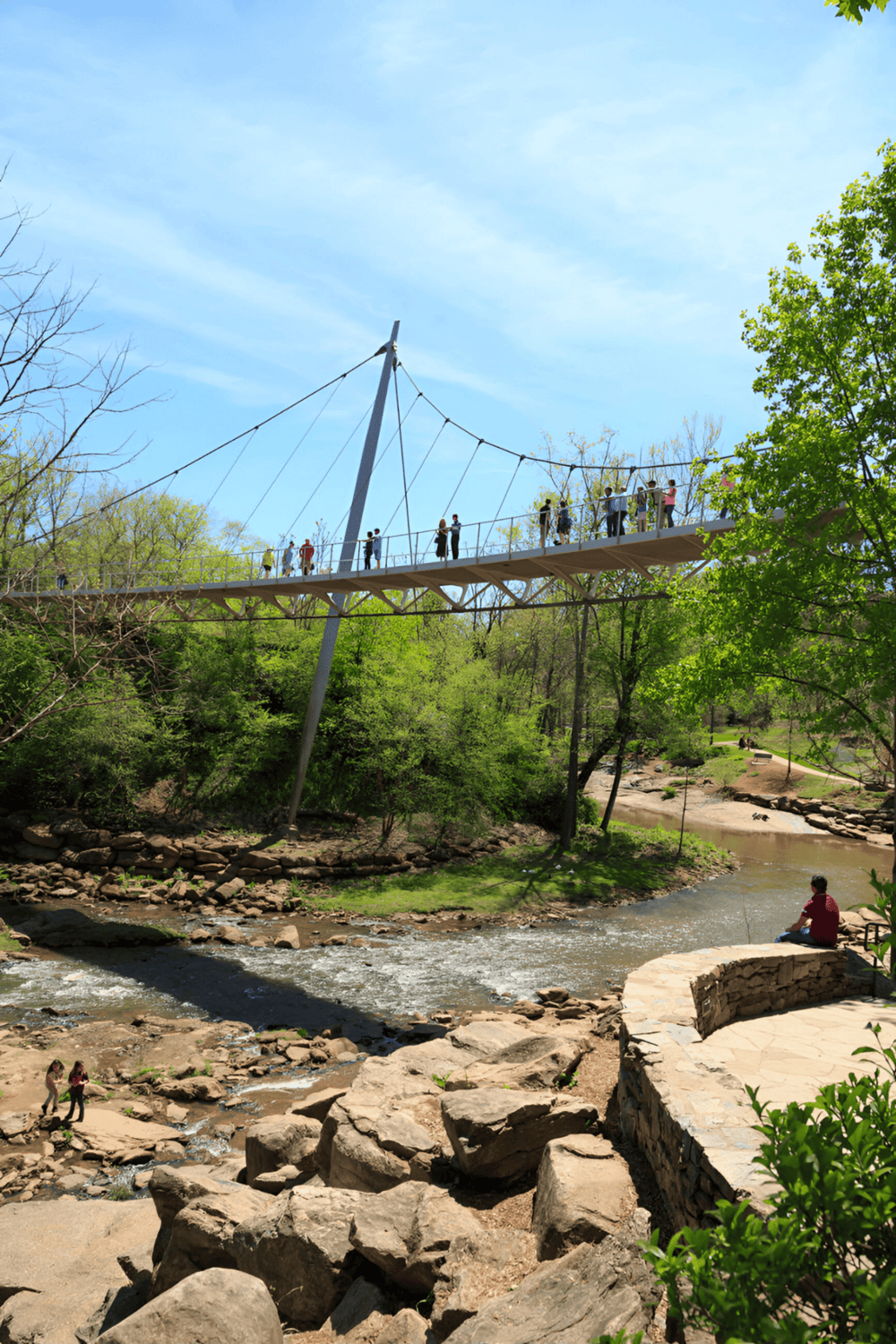 Enjoy the adventure on the Quest for Directions suspension bridge over a scenic river in lush green park.