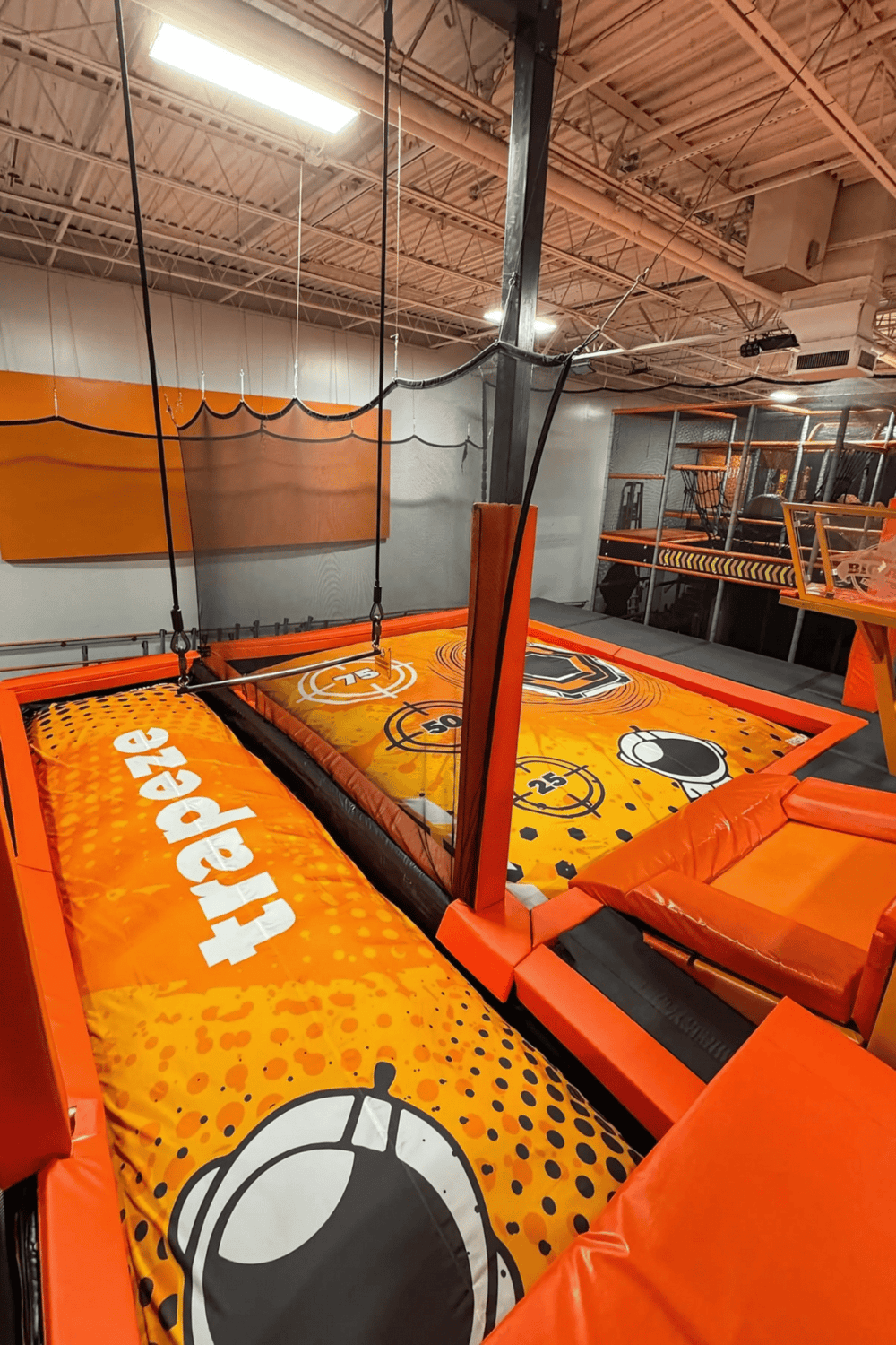 Indoor trampoline park with orange padded flooring and basketball hoops for active entertainment.