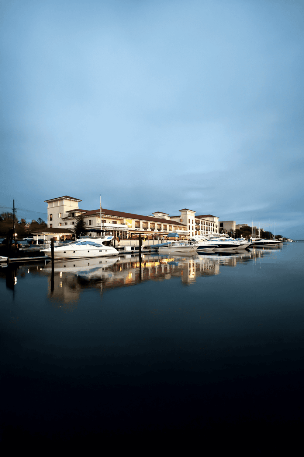 Luxurious yacht marina at dusk with calm waters and waterfront hotel, ideal for travel and leisure.