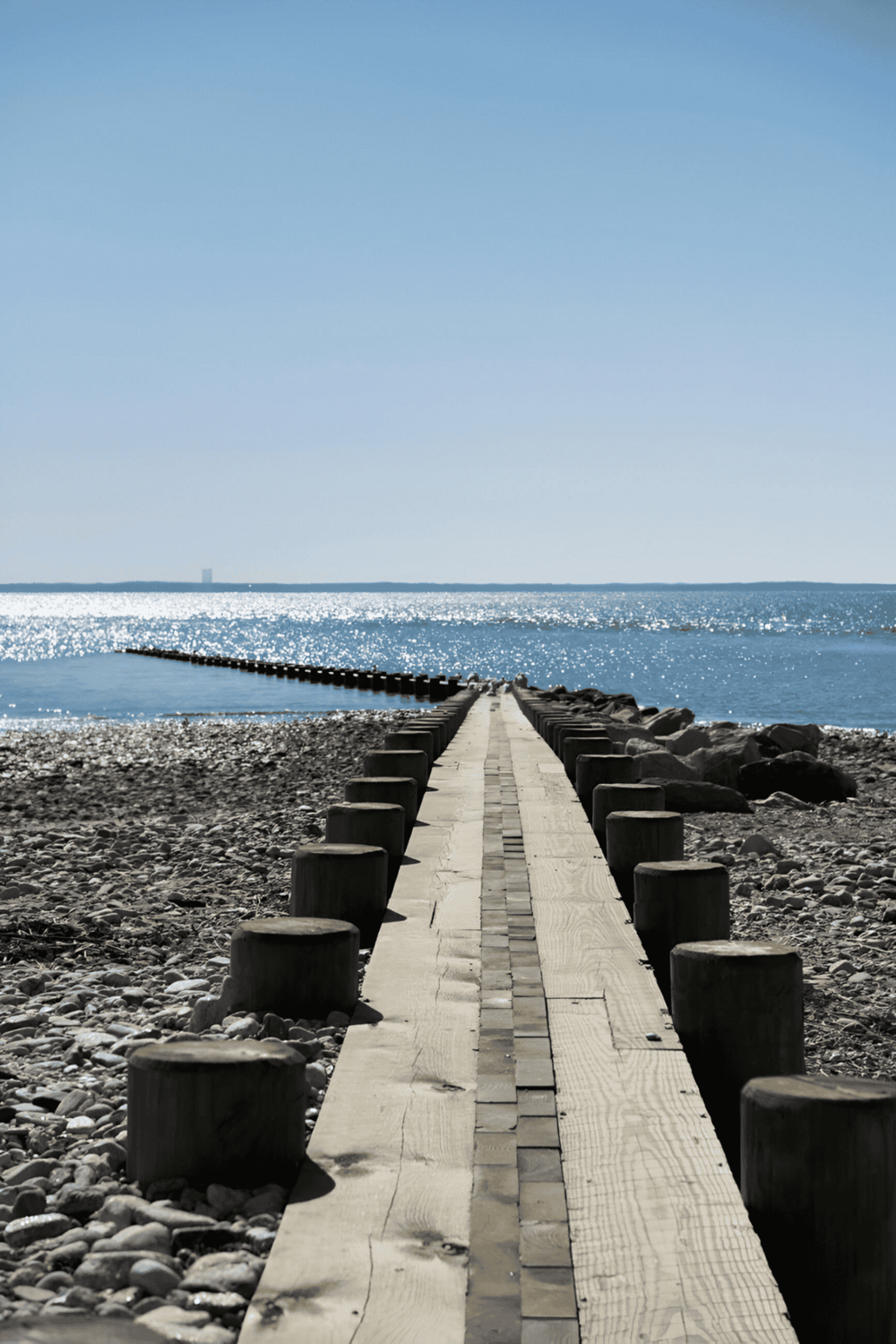 Seaside wooden pier extending into the ocean under clear blue sky.