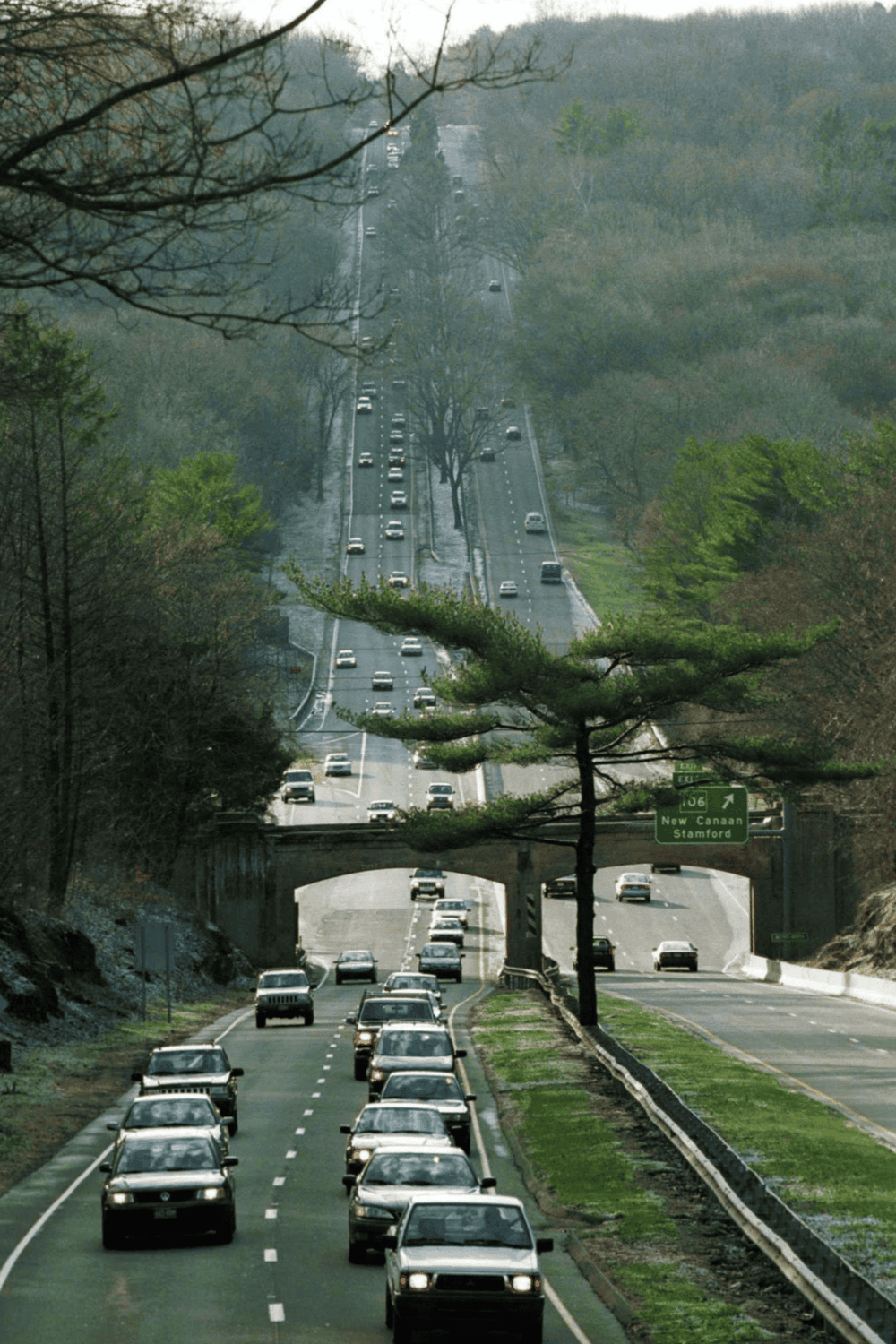 Vehicles on scenic highway with lush green trees and mountainous background.