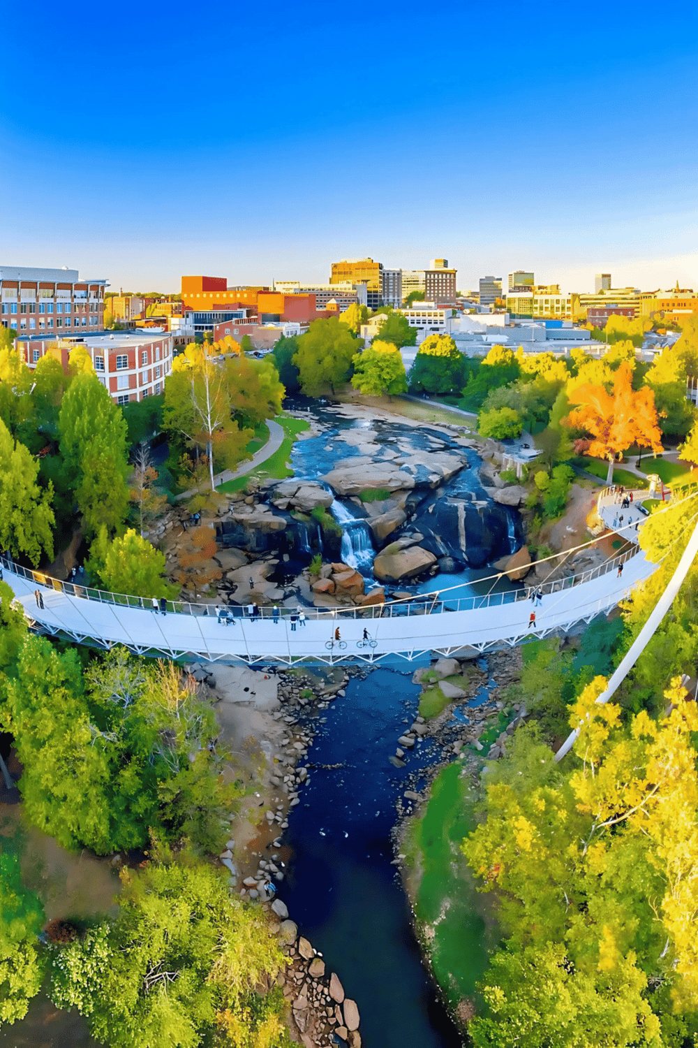 Breathtaking aerial view of downtown with a scenic waterfall and a modern pedestrian bridge during daytime.