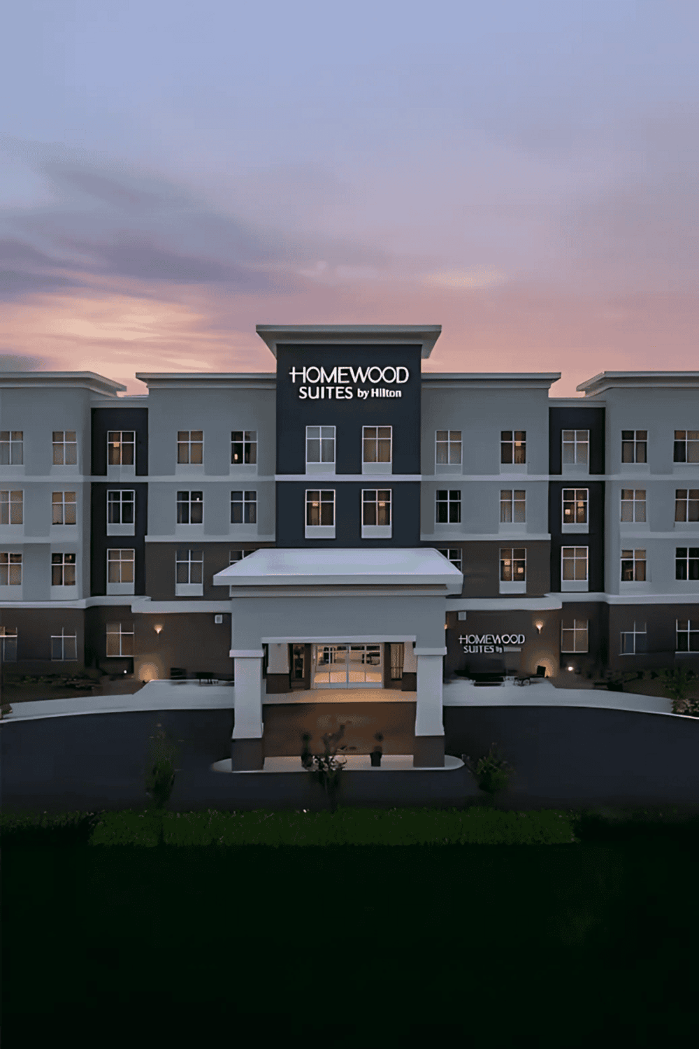 Modern Homewood Suites hotel exterior at dusk, showcasing Hilton-branded accommodations for travelers.