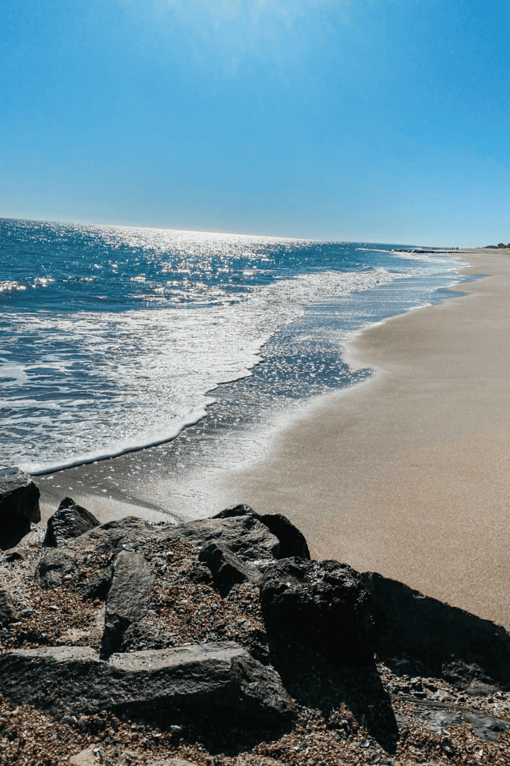 Aerial view of a sunny beach with turquoise ocean waves hitting the sandy shore.