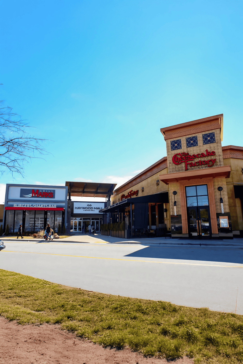 Outdoor shopping mall featuring The Cheesecake Factory and Grill Marks restaurant, with clear blue sky.