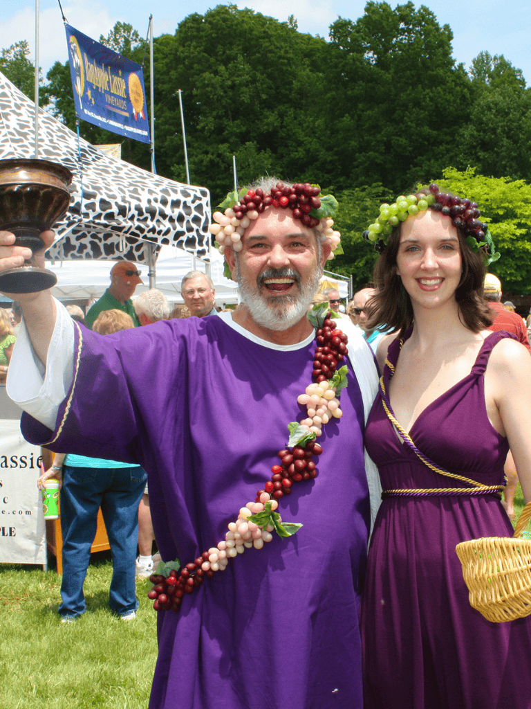 Vineyard festival celebration with people wearing grape-themed crowns and costumes outdoors.