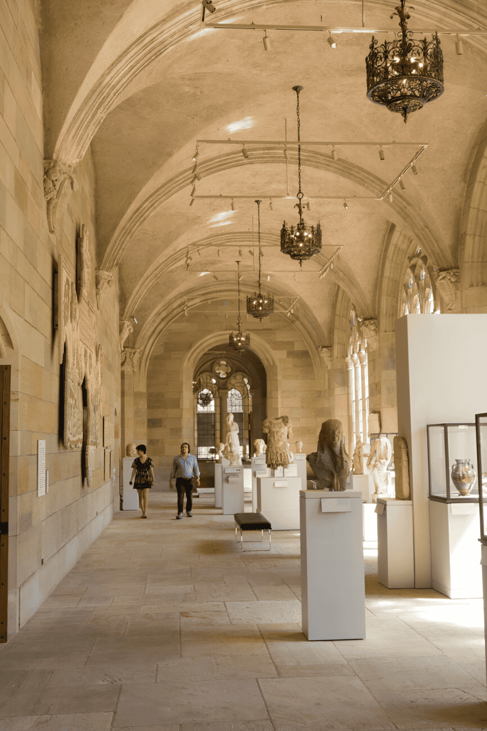 Ancient sculpture art display in a historic museum with arched ceilings and elegant chandeliers.
