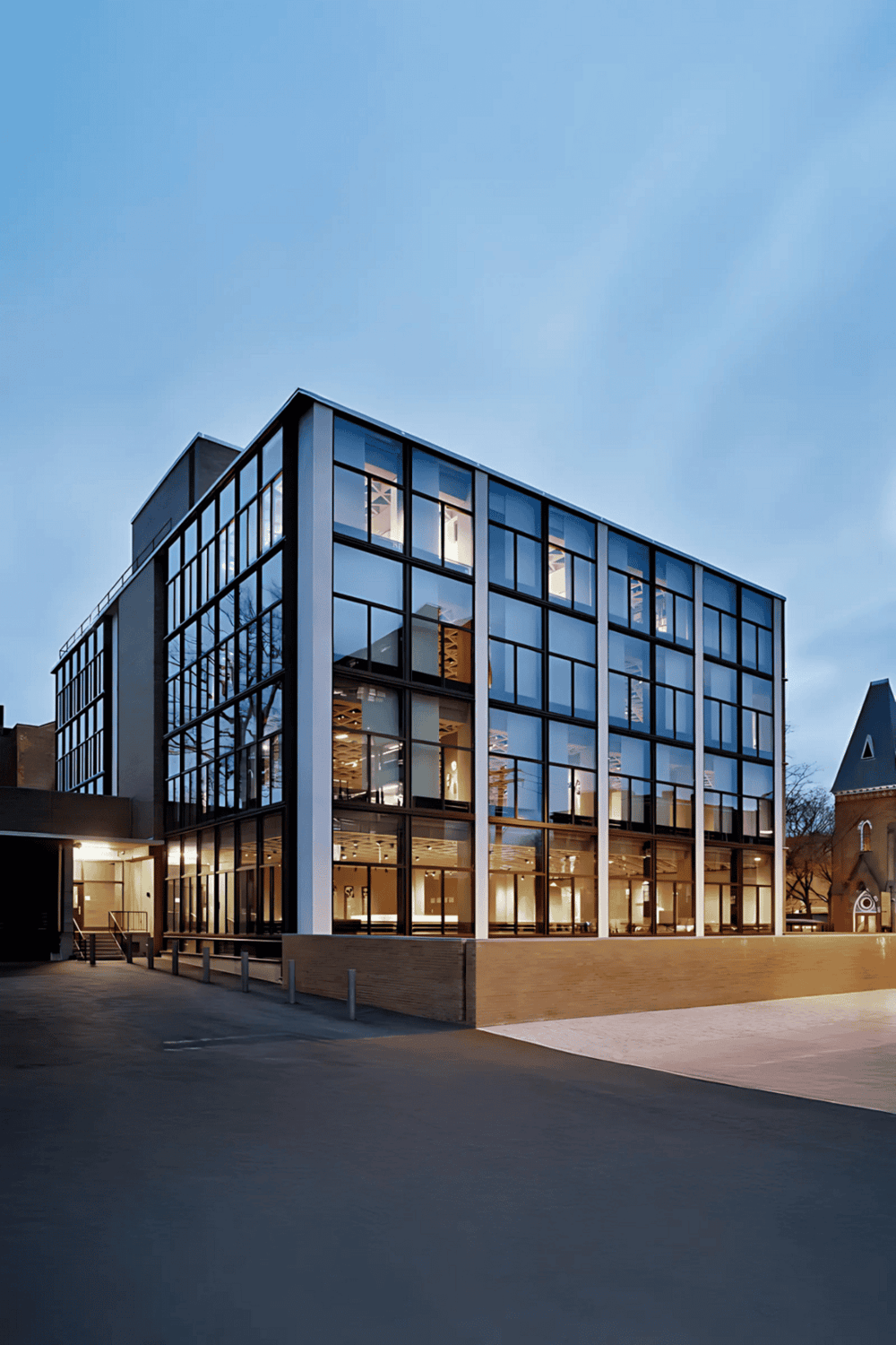 Modern office building with glass facade and illuminated interior at dusk.