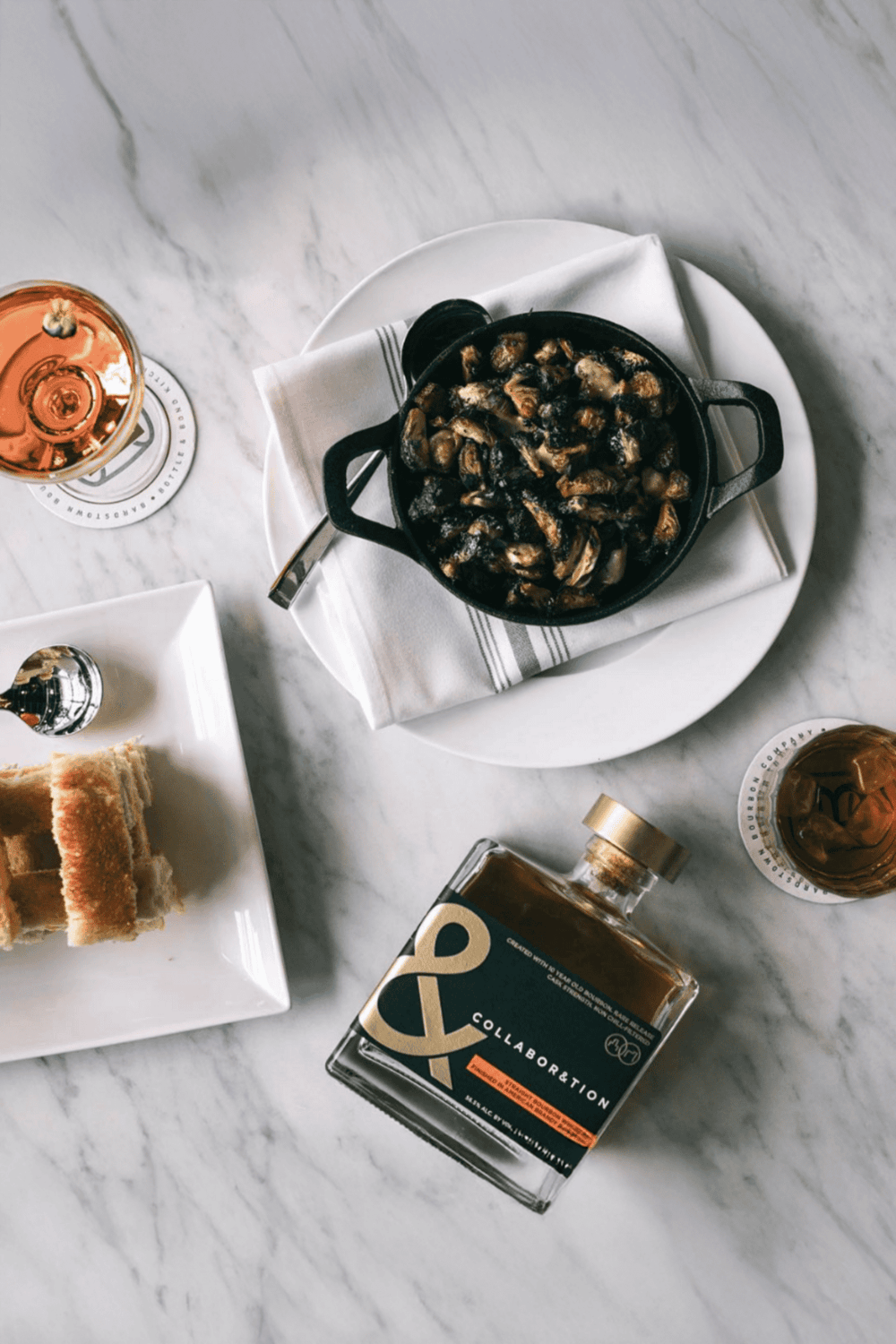 Canned mushrooms dish served with drinks and snacks on marble table.