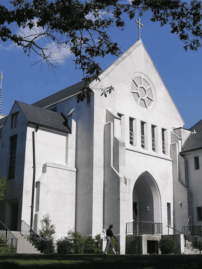 Bright white church with gothic architecture and stained glass windows, against a clear blue sky.