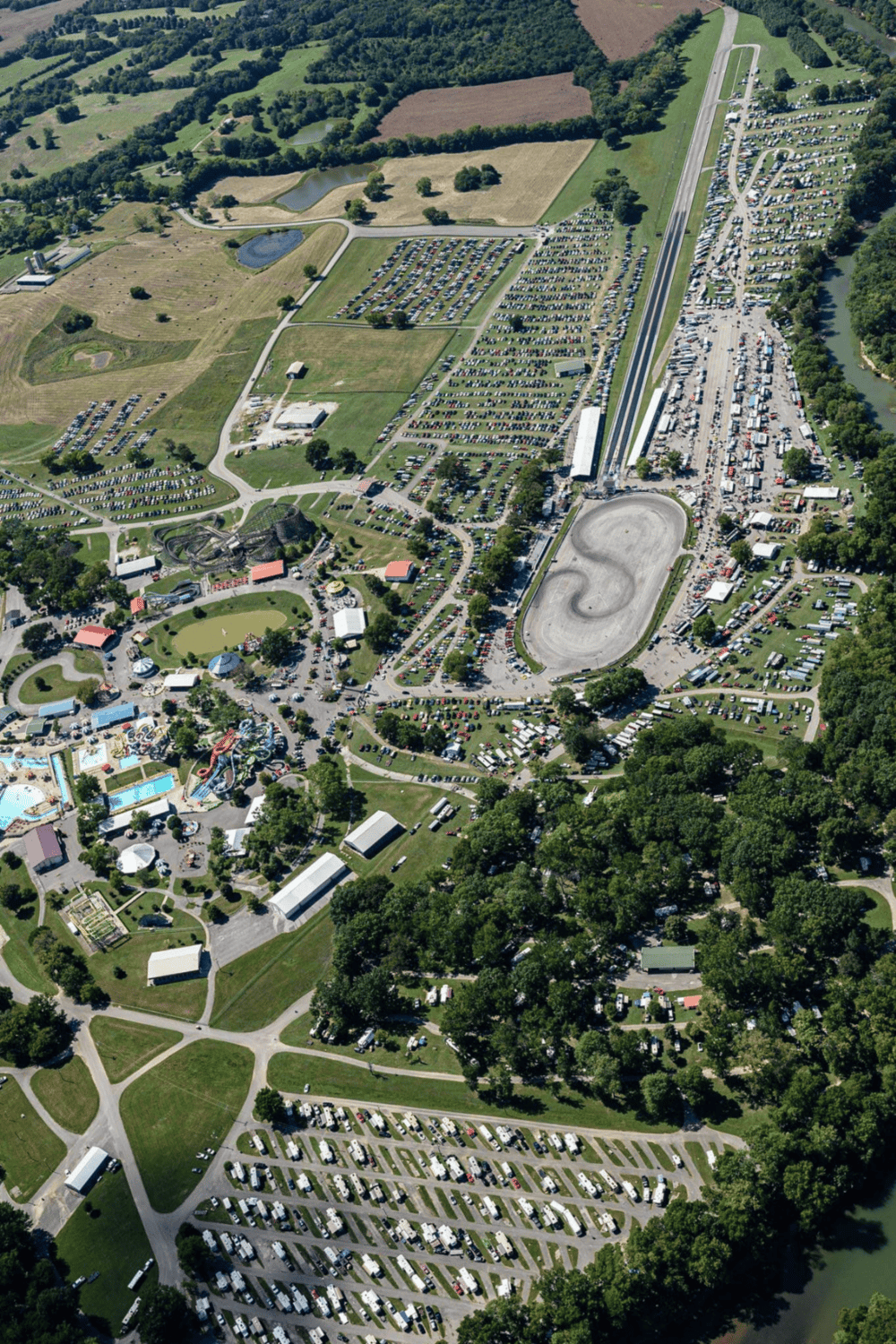 Amusement park with roller coasters, parking lots, water rides, and lush greenery from an aerial view.