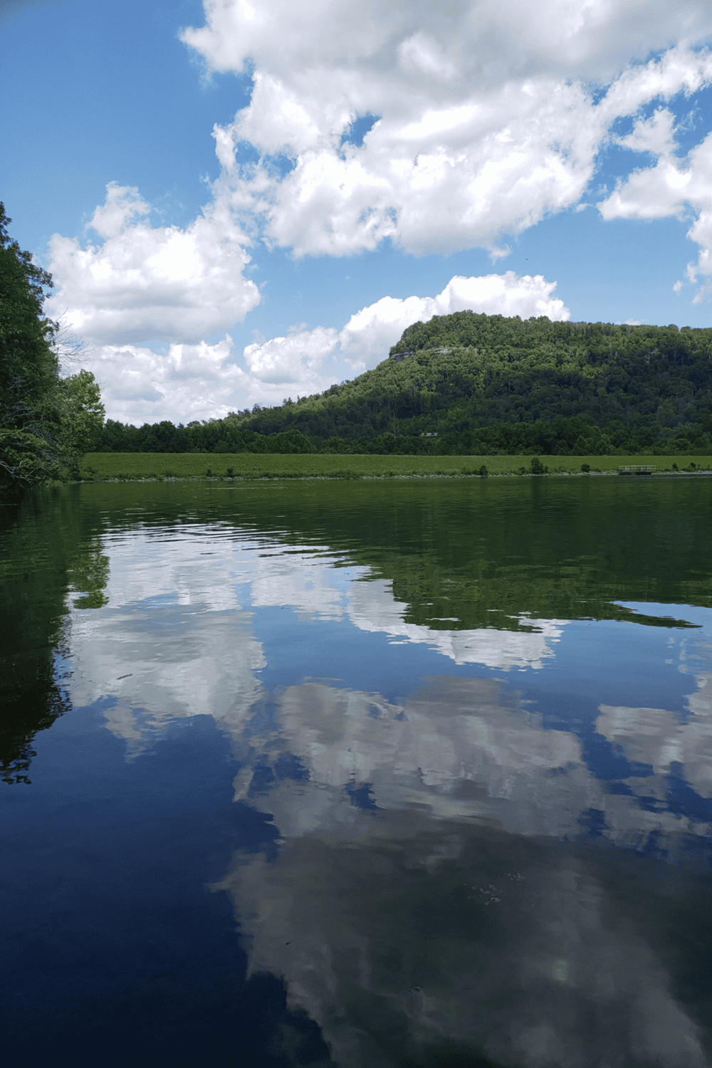 Serene river with mountain backdrop and cloudy sky, lush greenery, scenic outdoor environment.