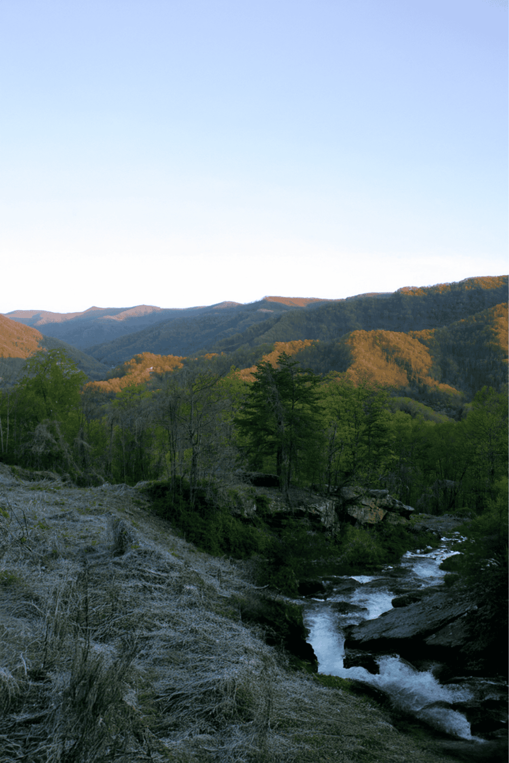 Serene mountain landscape with flowing river, lush green trees, and rolling hills, perfect for outdoor adventures and nature exploration.