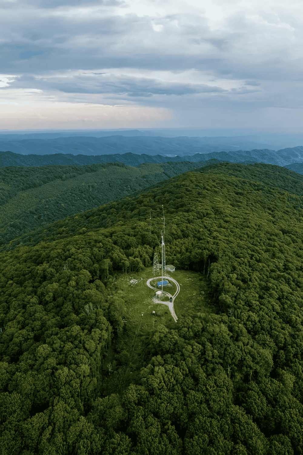 Elevated view of a lush green mountain landscape with communication tower and research station.