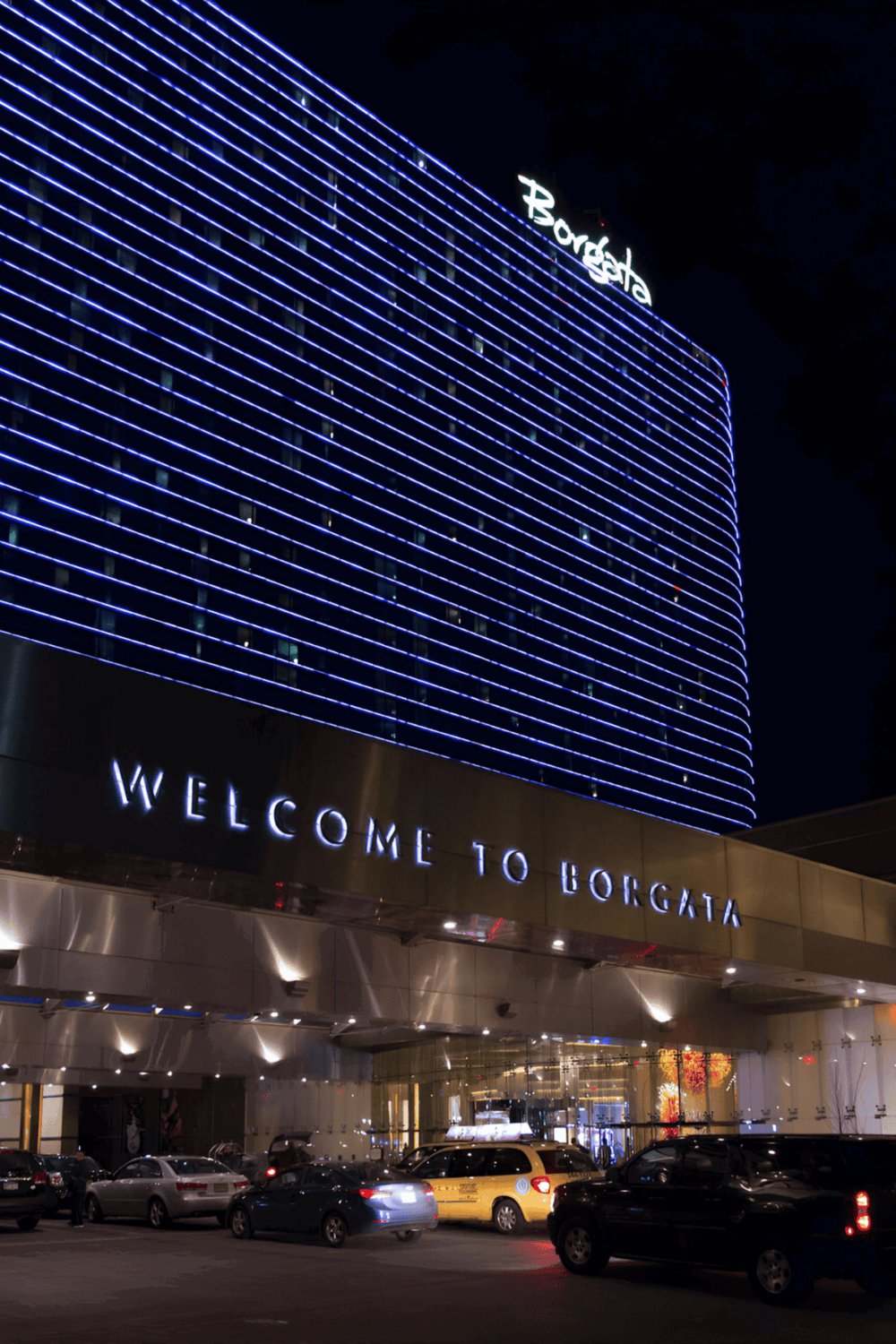 Brightly lit Borgata Hotel at night with neon blue stripes and welcoming signage.