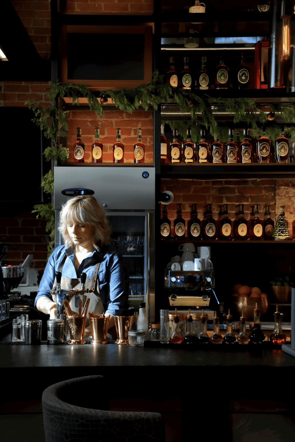 Herbal liquor bottles on shelves in a cozy bar setting with festive greenery and warm lighting.
