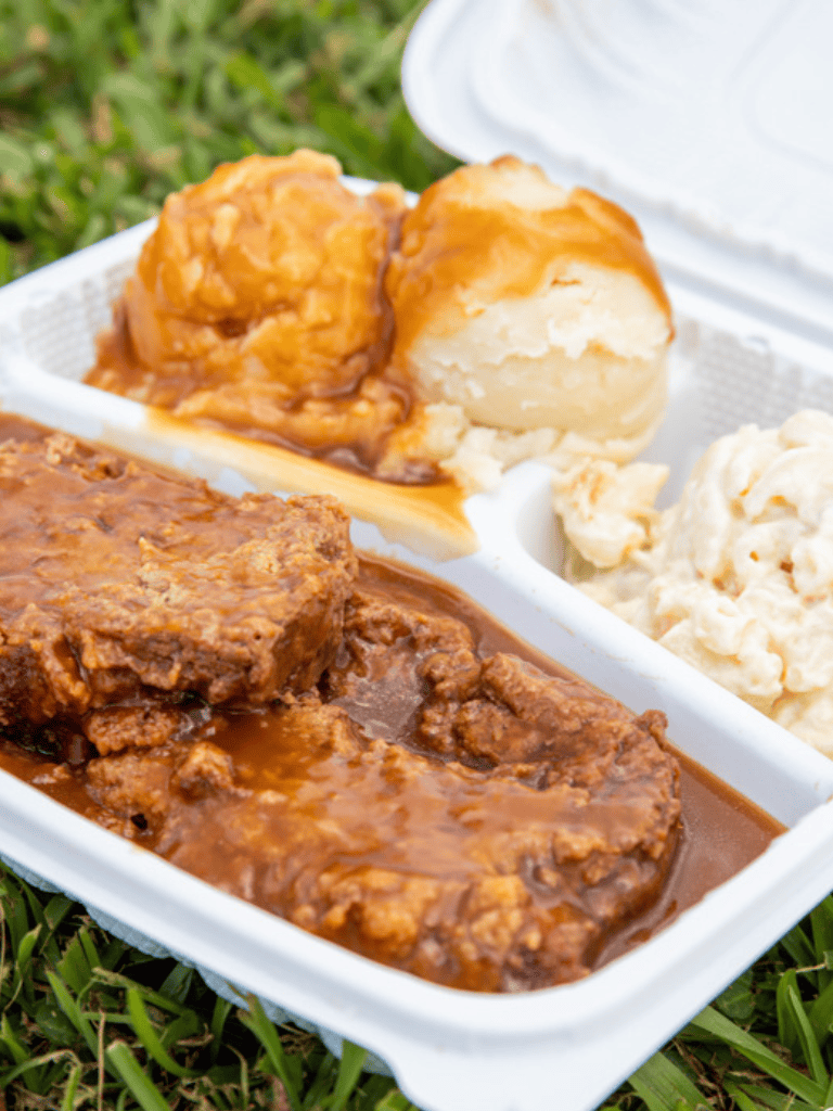 Savory beef stew with mashed potatoes, gravy, and cornbread in biodegradable container.