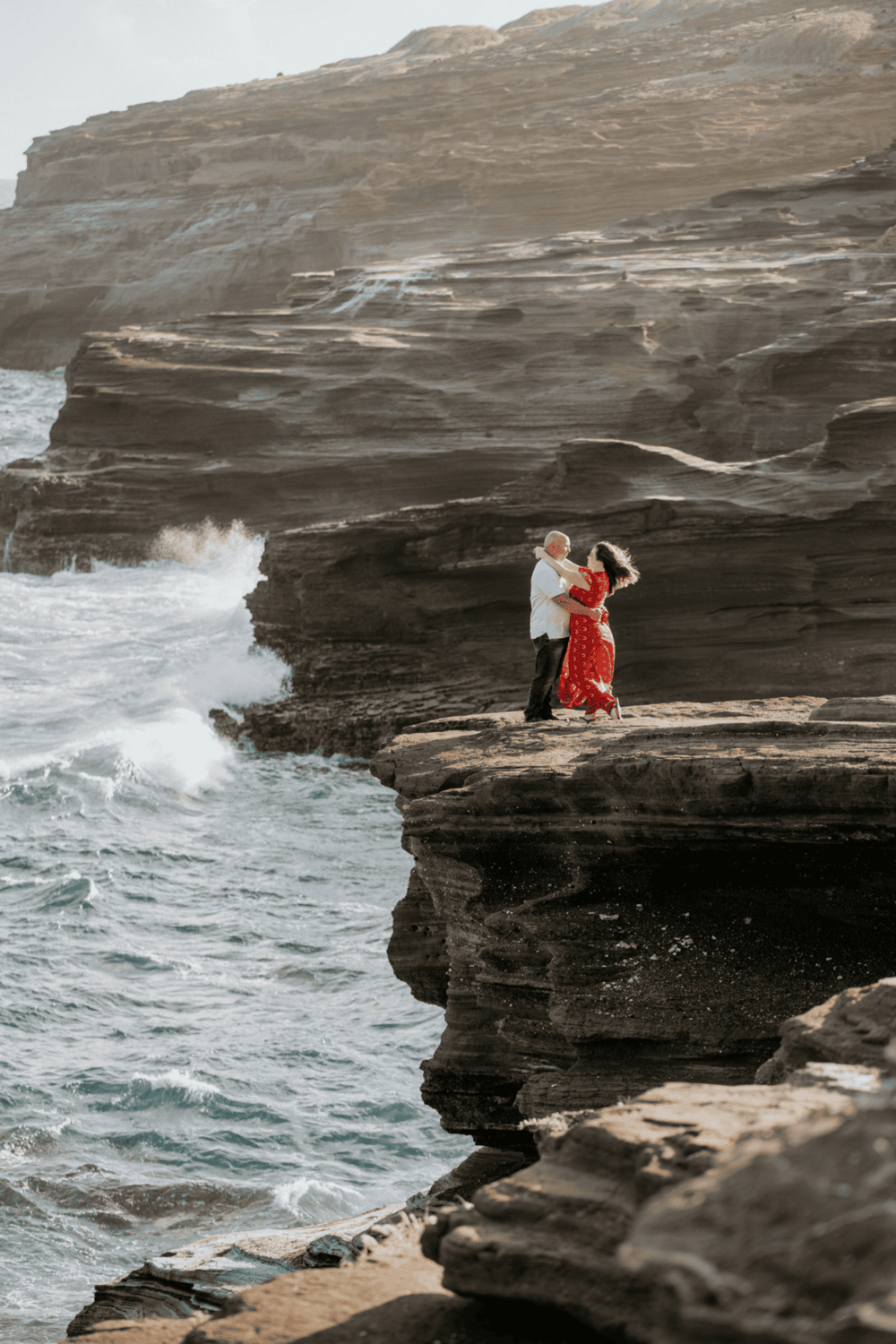 Seaside couple dancing on coastal rocky cliffs with ocean waves in the background.