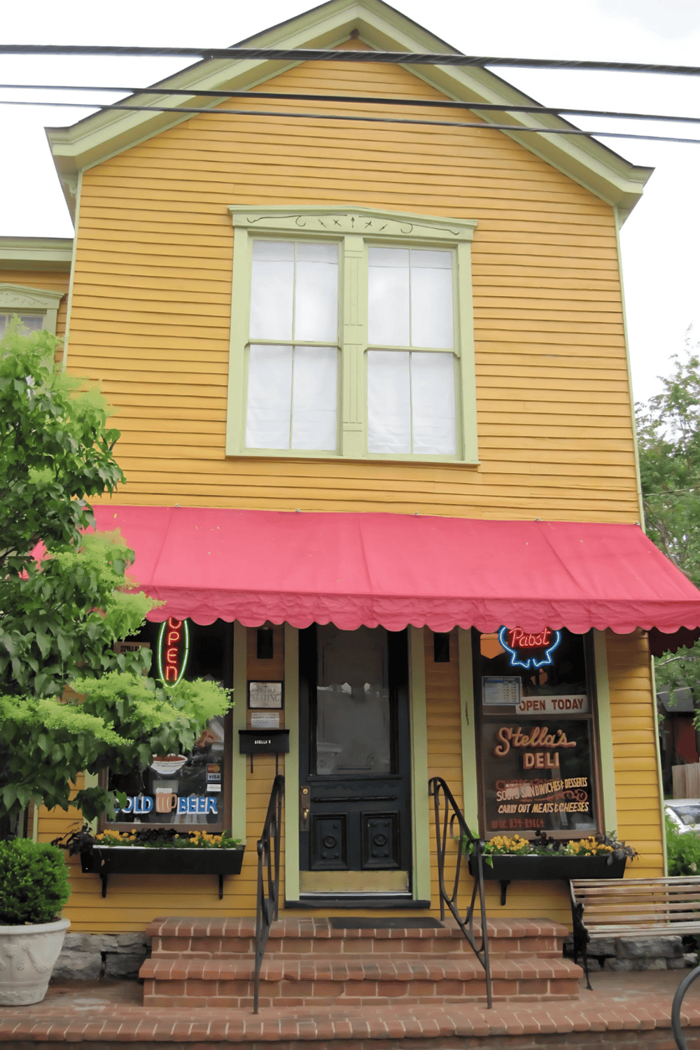 Cozy yellow building housing Stella's Deli with red awning, offering sandwiches, desserts, and craft beers.