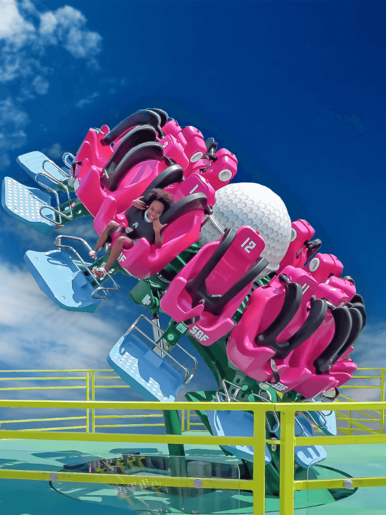 Thrill ride at amusement park with a giant golf ball and pink seats, fun family amusement park attraction.