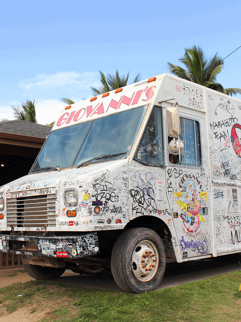 Graffiti-covered food truck parked outdoors with palm trees in background.