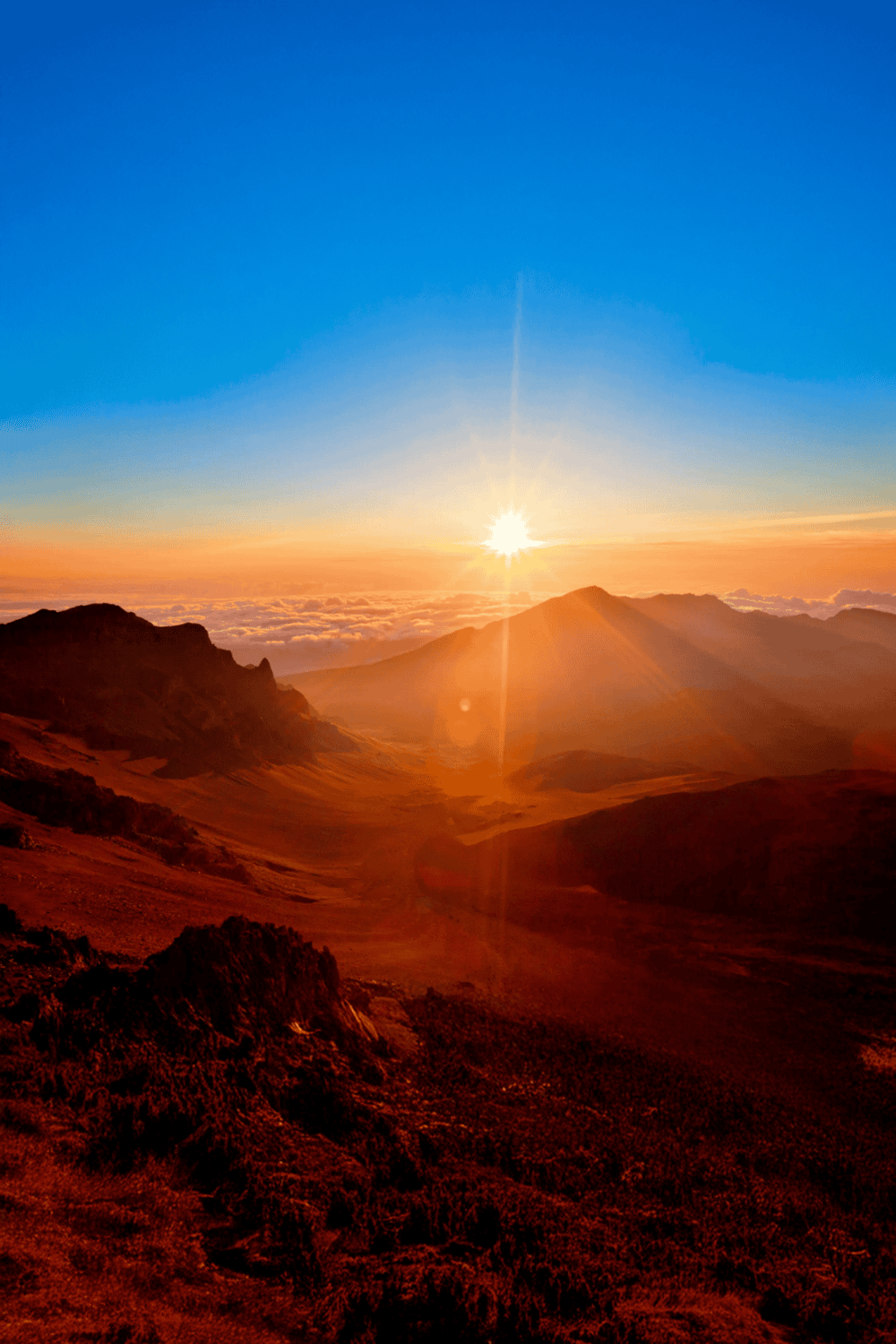 Vibrant sunrise over mountain landscape with bright blue sky and clouds, showcasing breathtaking natural scenery.