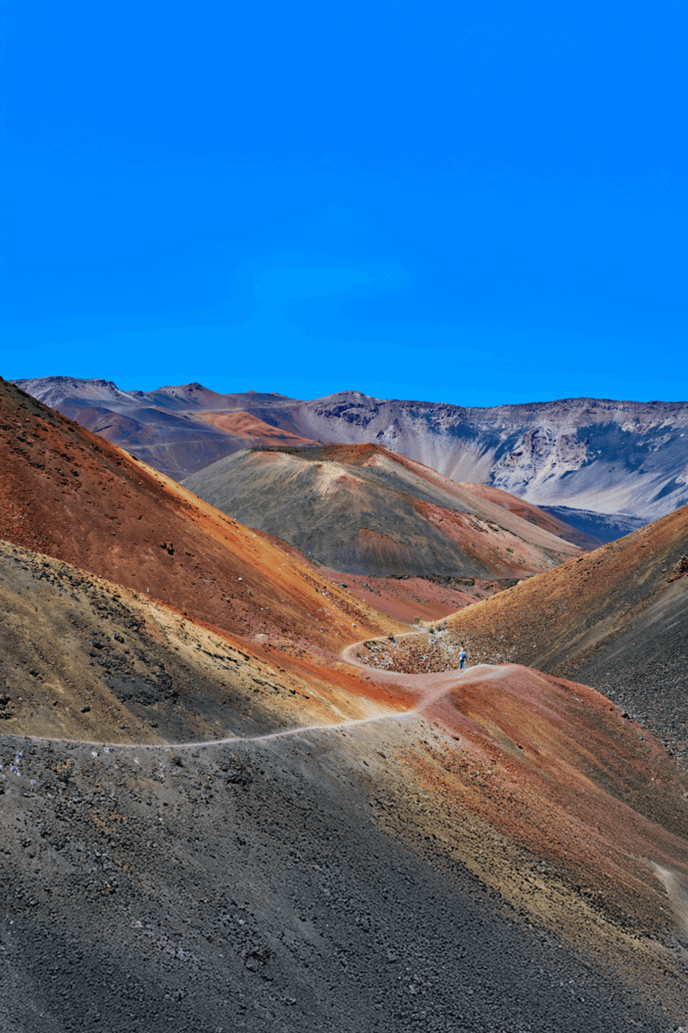 Colorful mountain landscape with a winding trail, vibrant terrain, and clear blue sky, perfect for adventure travel imagery.