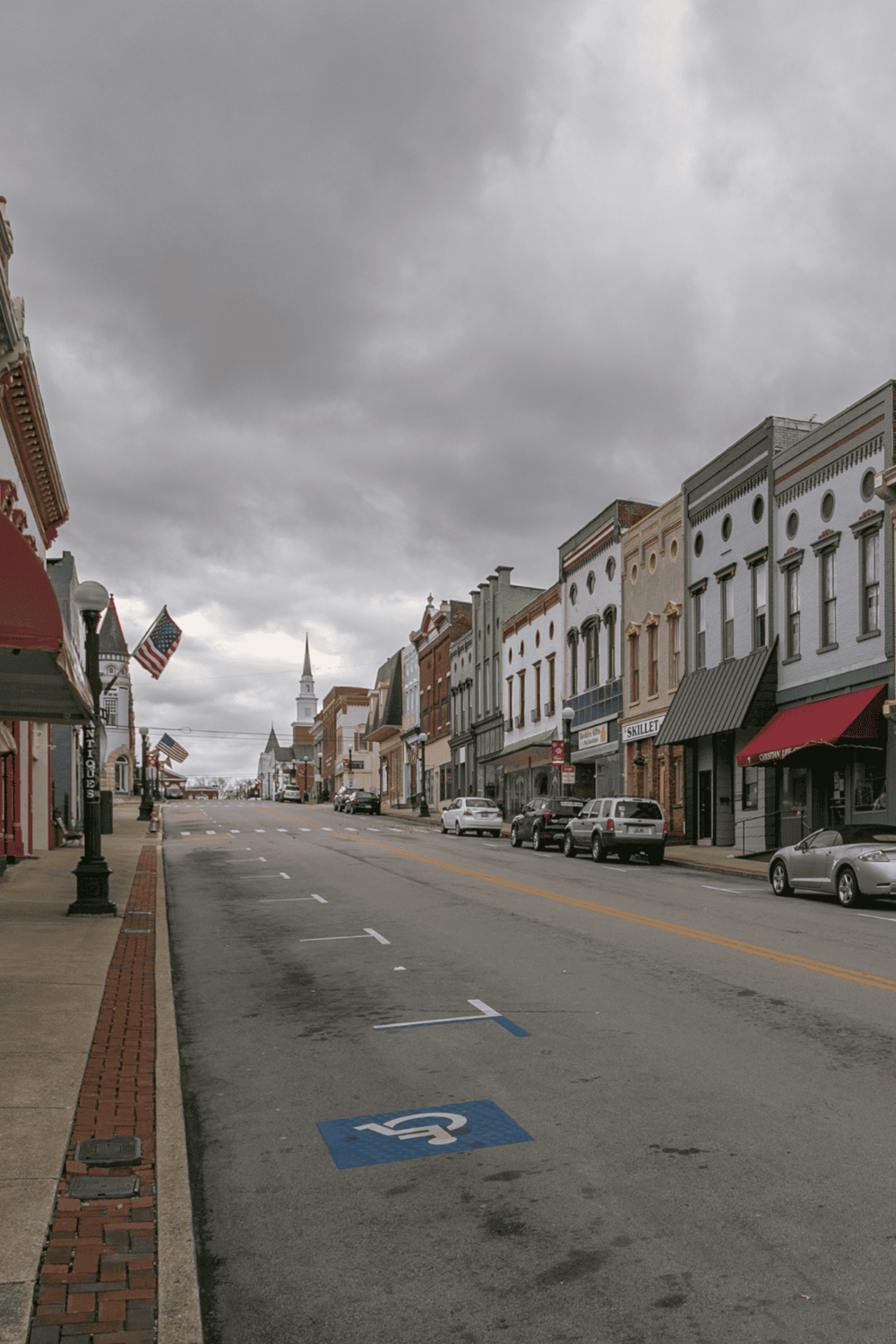 Downtown historic street with shops, American flags, and gloomy sky in small town.