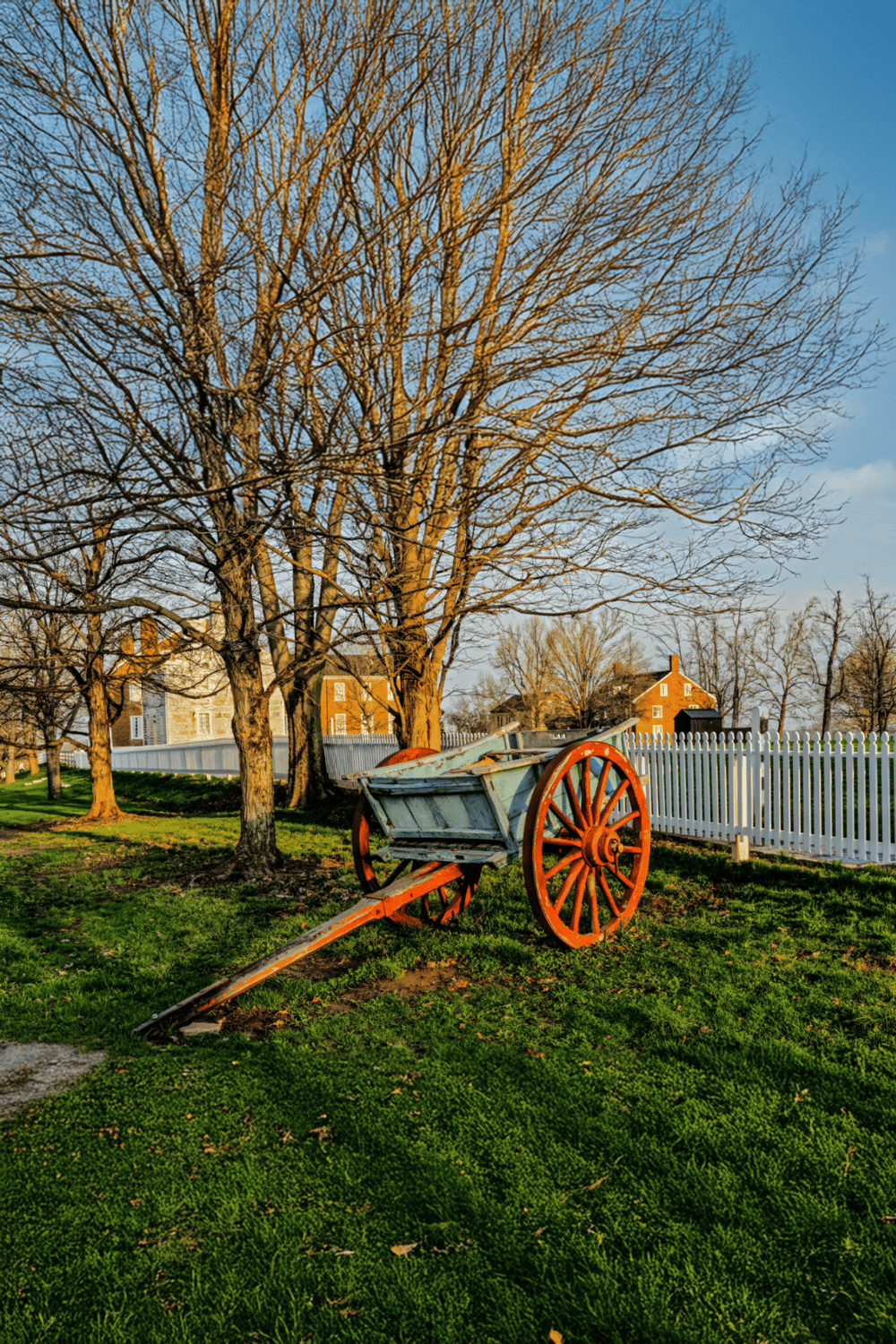 A historic wooden wagon beneath leafless trees in a picturesque park scene.