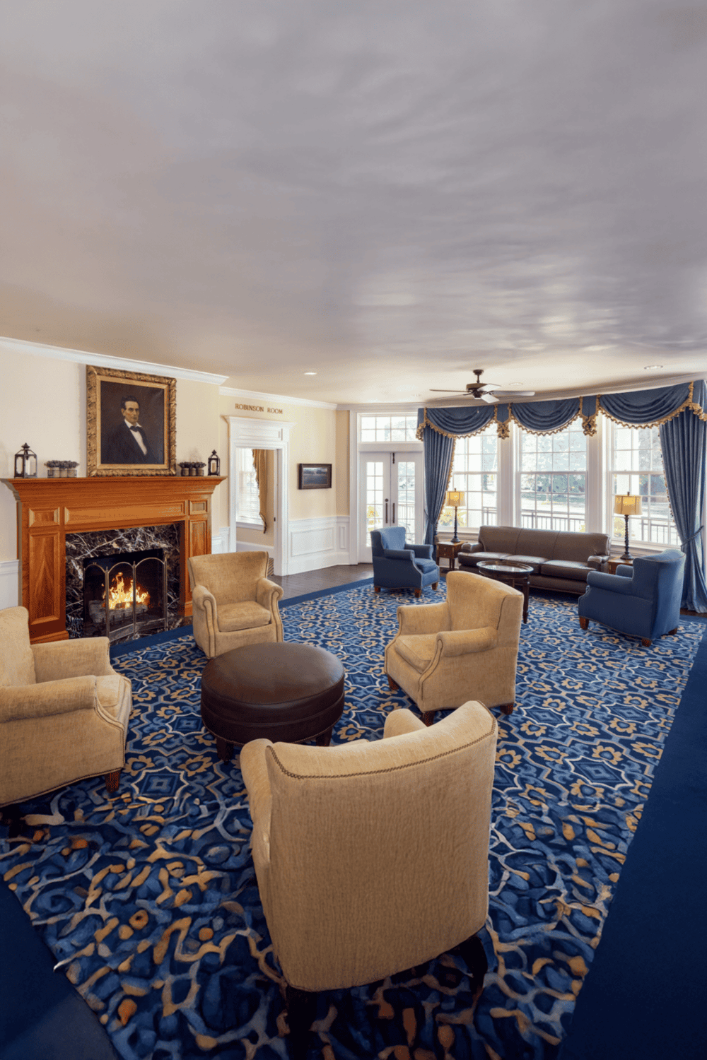 Cozy hotel lobby with fireplace, classic armchairs, and elegant blue drapes, offering a welcoming atmosphere.