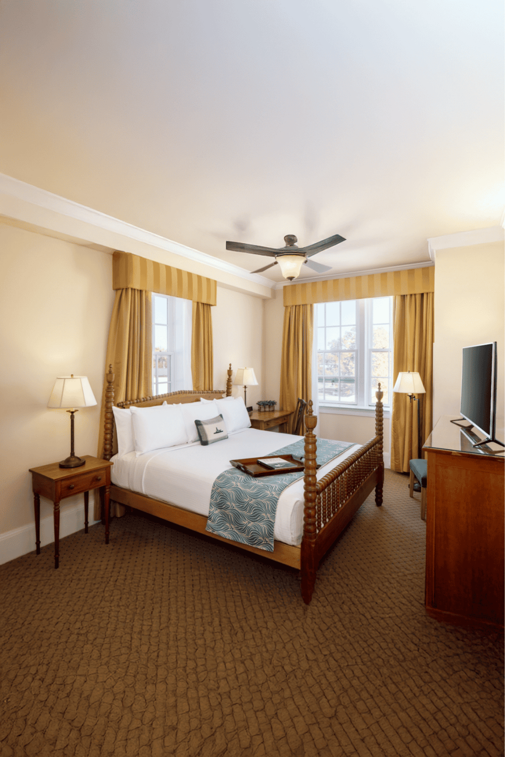 Comfortable hotel bedroom with wooden furniture, large windows, and cozy decor.