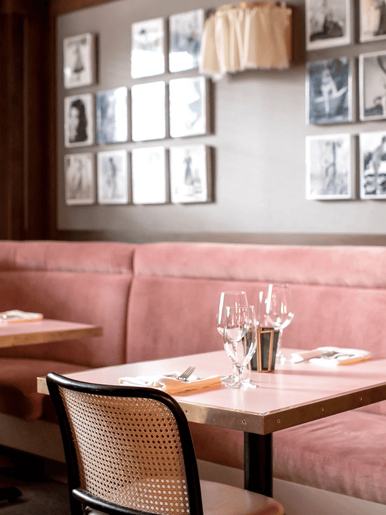 Cozy restaurant interior with pink seating, wine glasses, and wall art, ideal for a dining experience.