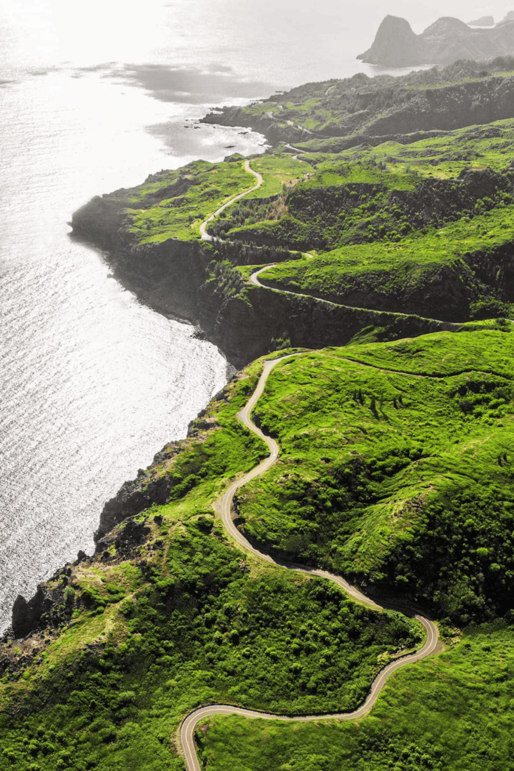 Winding coastal road through lush green cliffs and scenic ocean views.