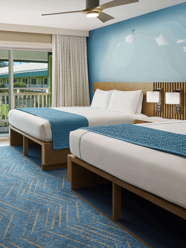 Cozy hotel room with two queen beds, blue accents, and balcony with ocean view.