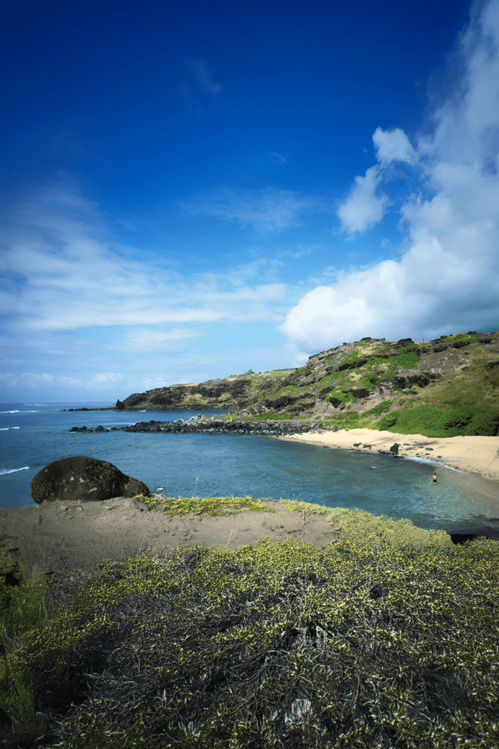 Coastal beach with rocky hills, clear blue sky, and ocean waves, scenic ocean view.