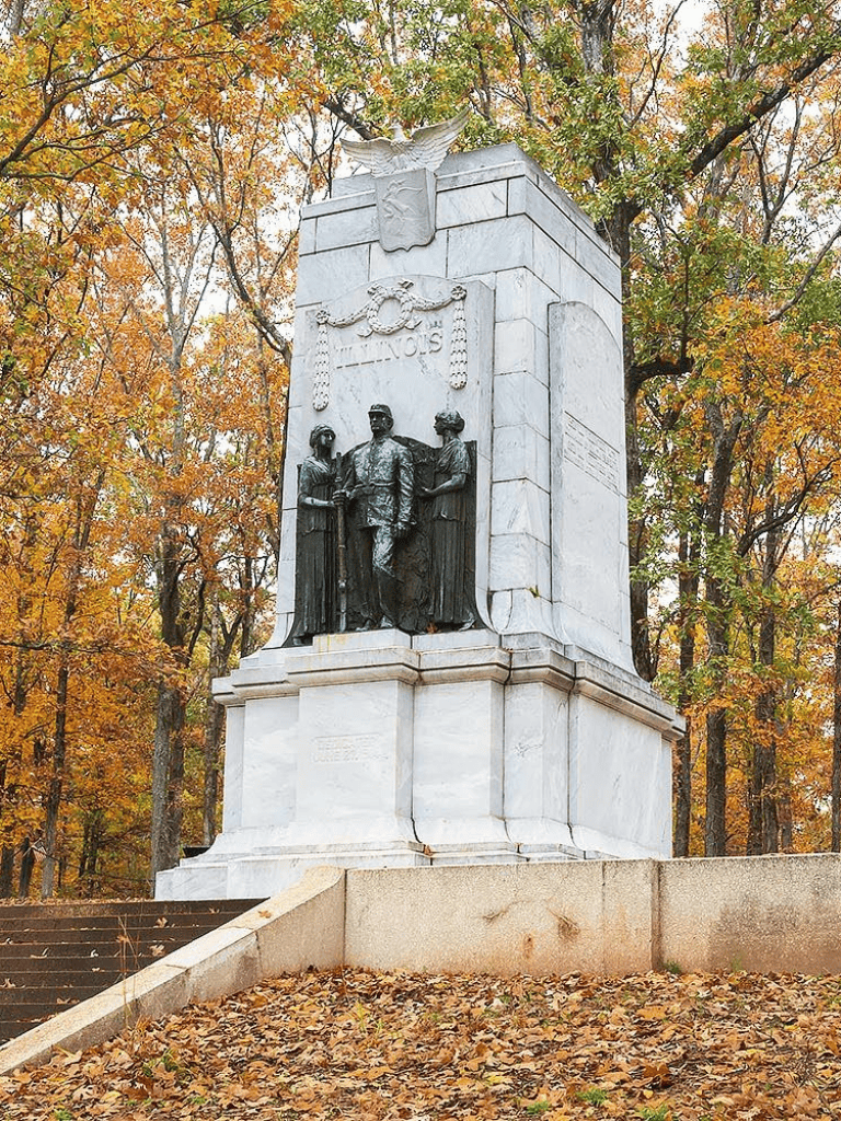 Bronze Civil War monument in a park during autumn with colorful leaves and trees in the background.