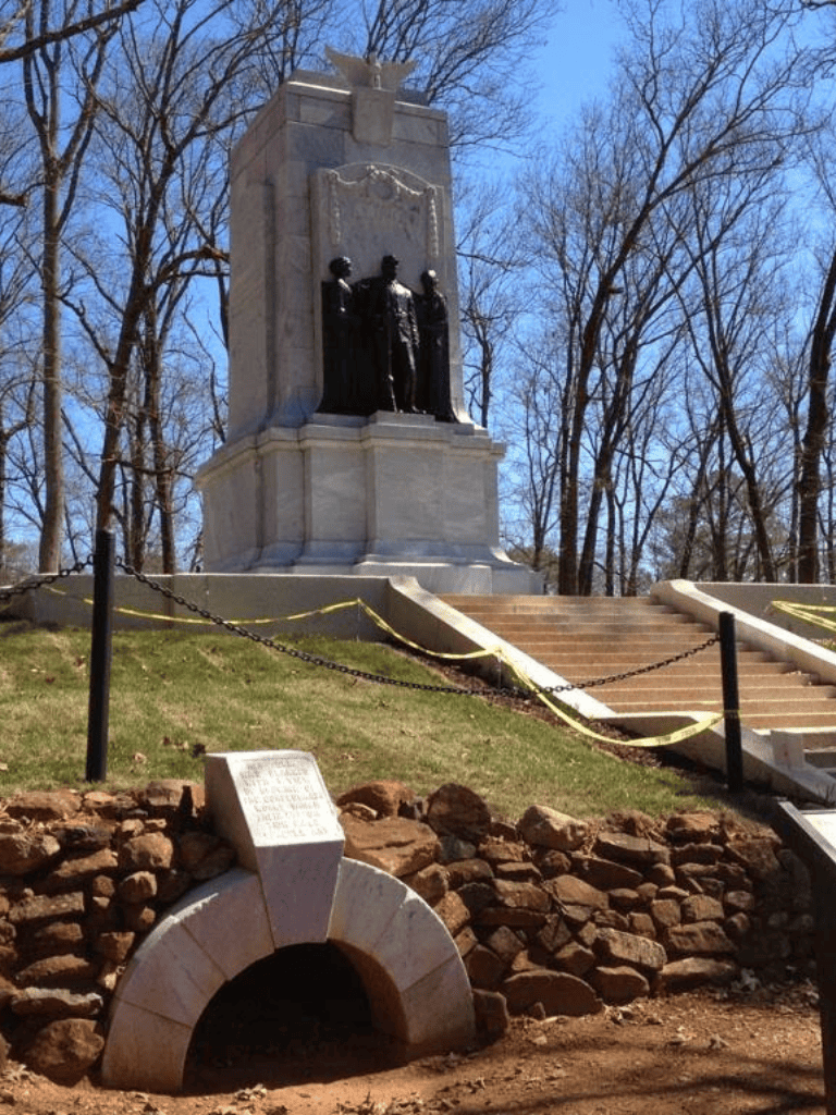Statue of three historical figures in a park with leafless trees and clear blue sky.