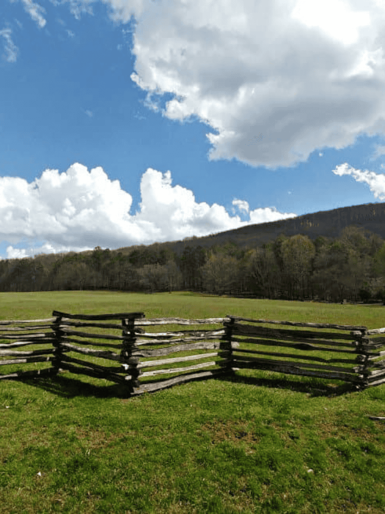 Rustic wooden fence on green field with scenic mountain and cloudy sky background.