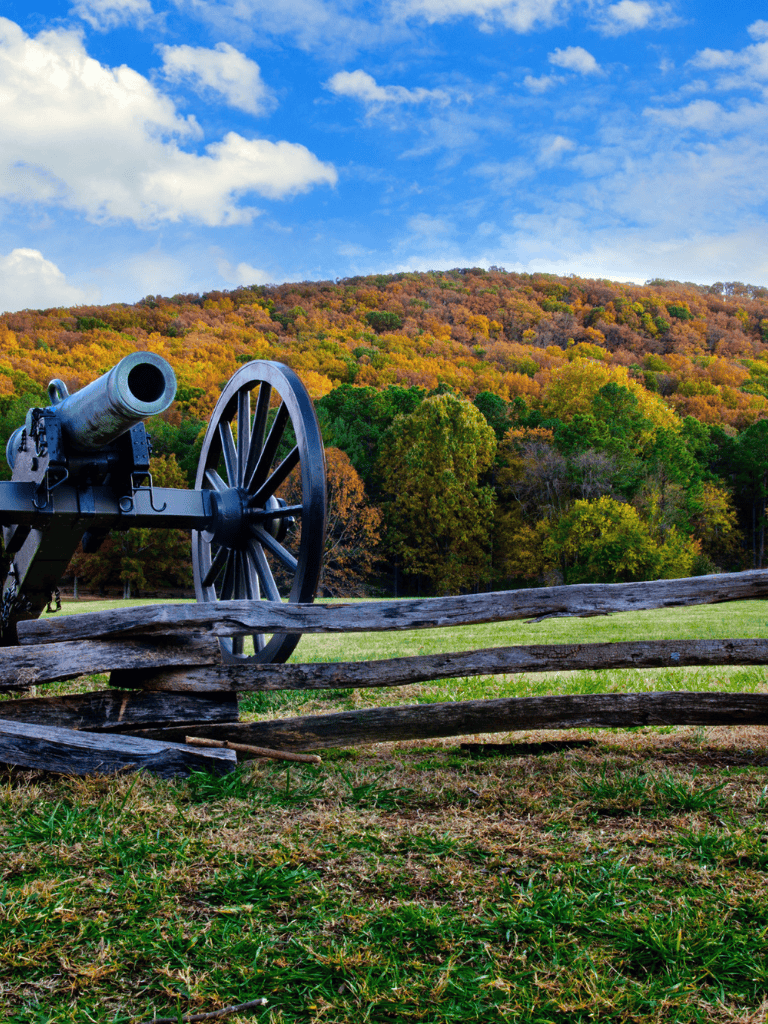 Historic cannon with scenic autumn mountain background and wooden fence in foreground.