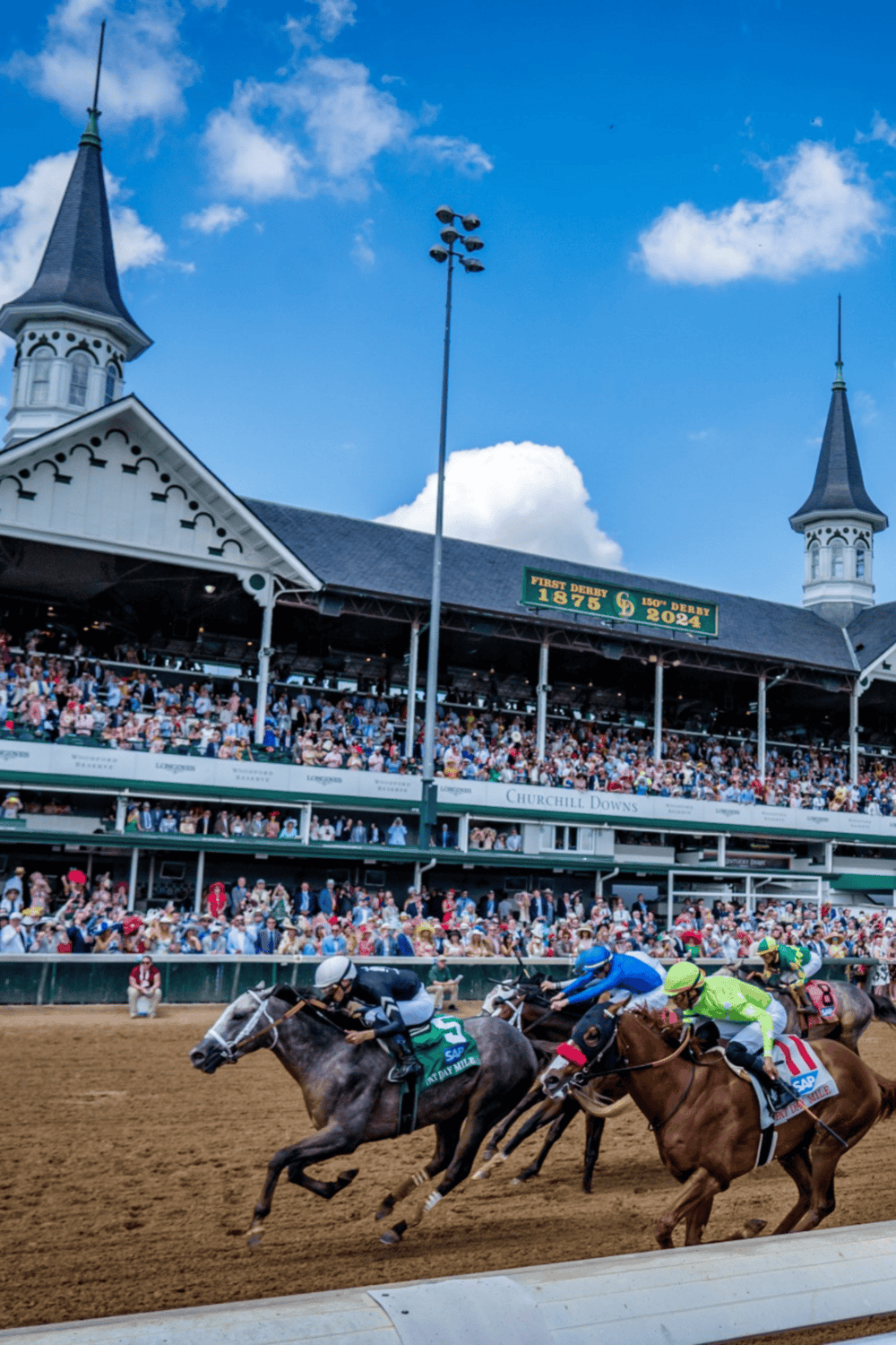 Fast horse race at Churchill Downs, historic Kentucky Derby venue, with cheering crowd and blue sky.