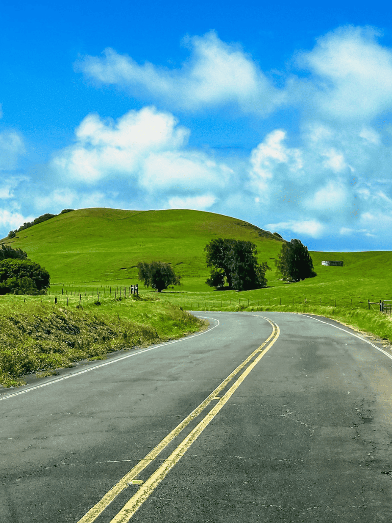 Rolling countryside road with green hills and blue sky, perfect for travel directions and scenic routes.