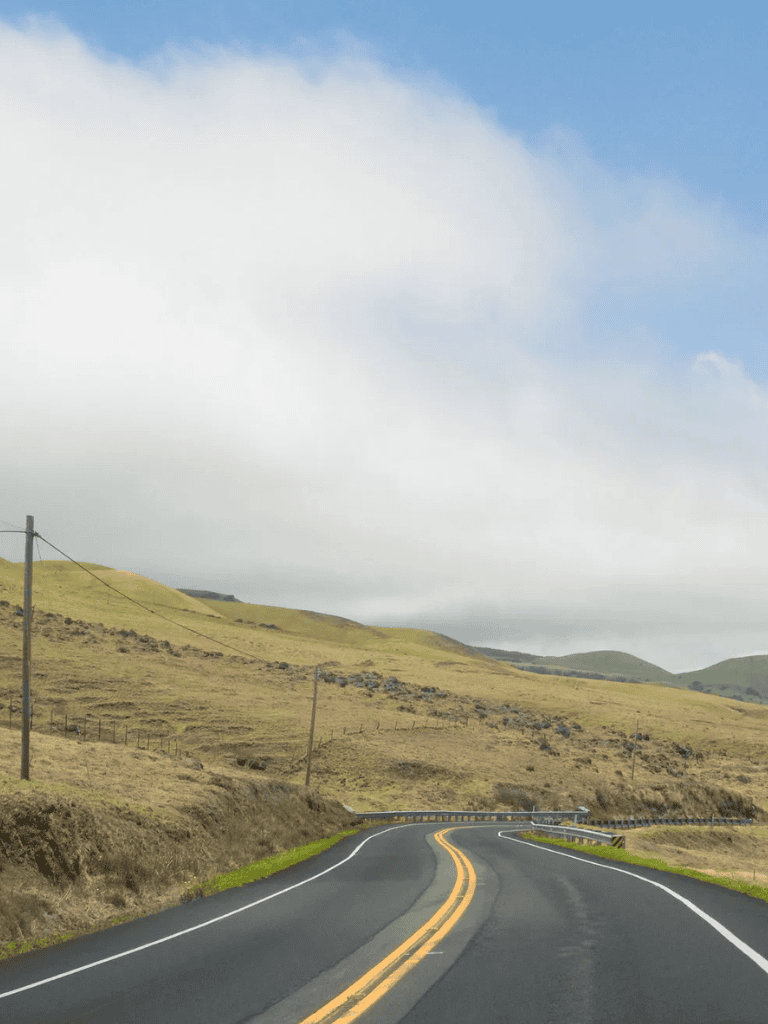 Open rural road with rolling hills and cloudy sky, ideal for scenic drives and adventure travel.
