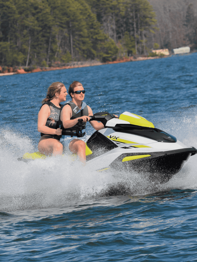 1. Two women riding a jet ski on a lake with trees in the background.