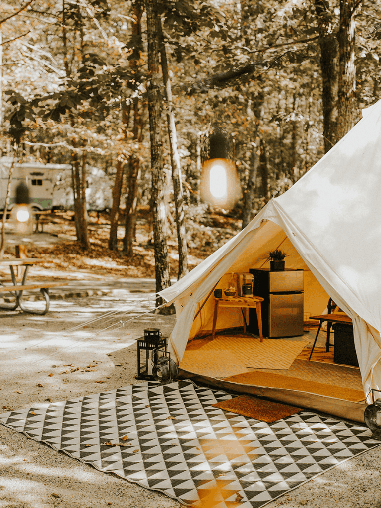 Cozy glamping tent set in a forested campsite with warm lighting and outdoor seating.